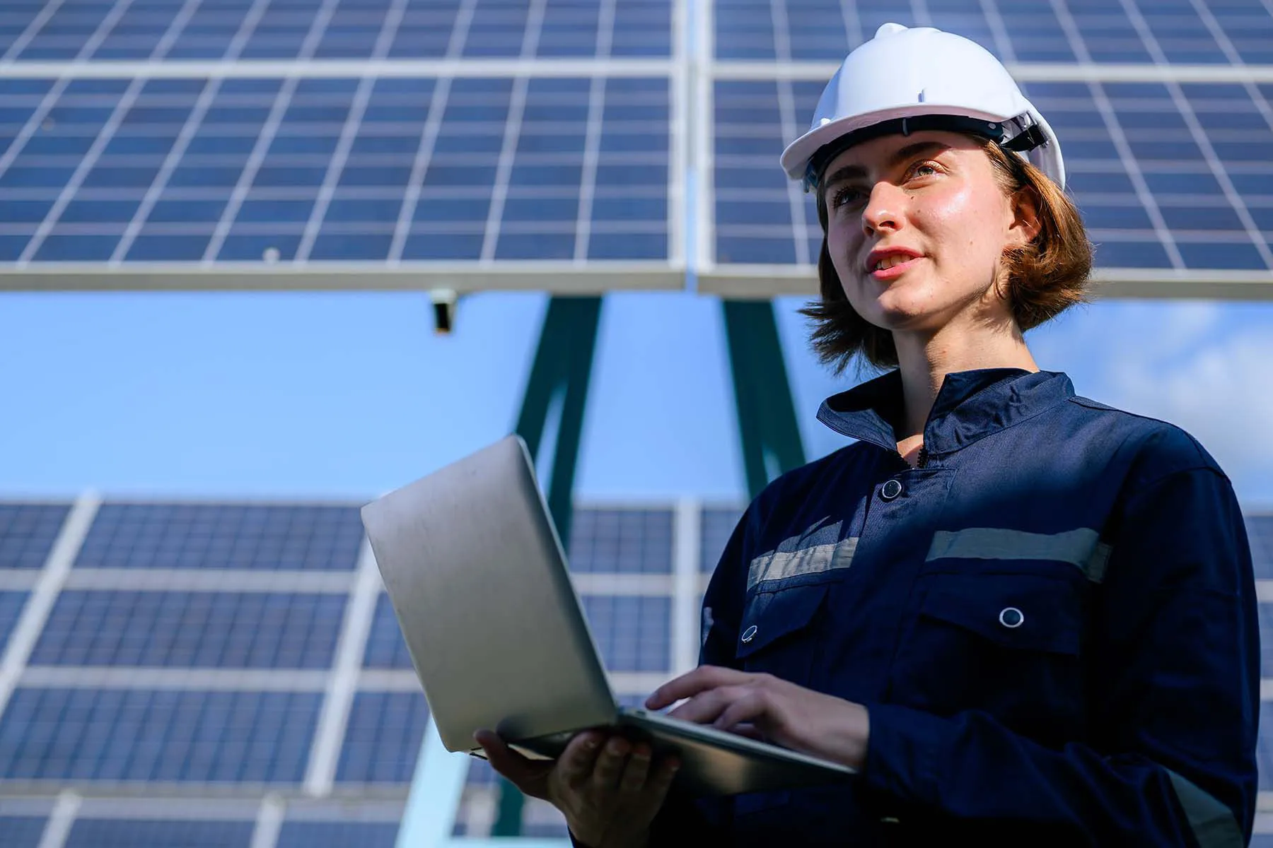 A VERBUND employee stands in front of a photovoltaic system with a laptop in her hand.